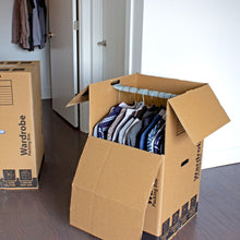Kraft wardrobe moving box opened with folded clothes visible, top flaps raised