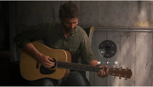 PlayStation 5 game screenshot: man strumming an acoustic guitar indoors