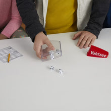 Yahtzee dice game score sheet with dice on table and hands holding dice