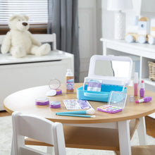 Pretend makeup play set on a table with open blue case, mirror, palettes, and lipsticks
