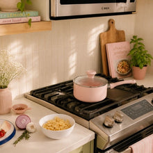 Pink ceramic non-stick saucepan with glass lid on black gas stovetop