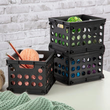 Black plastic storage crate with circular holes and open front, nested with another bin