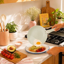 Pale green ceramic non-stick fry pan with sunny-side egg, on gas cooktop
