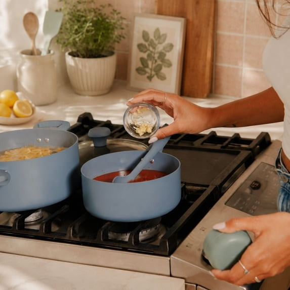 Blue ceramic non-stick sauce pan on gas stove with lid and spoon