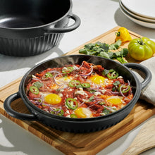 Black enameled Dutch oven with lid off, filled with baked dish in skillet-style pot.