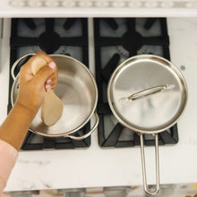 Two stainless pots on an electric stove grate, with child's hand