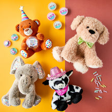 Tan bear plush with rainbow party hat and glowing music globe, with other toys nearby.