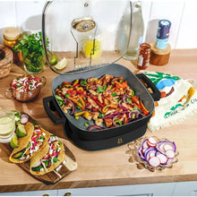 Electric skillet with glass lid over cooked vegetables in a black pan