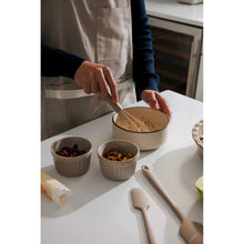 Taupe ceramic bakeware cups and ramekin, filled with ingredients on a prep table
