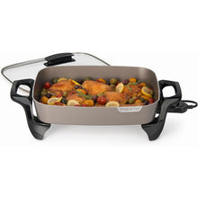 Grey ceramic electric skillet with lid and black handles, food cooking inside