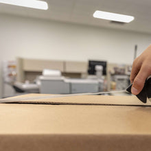 Hands applying clear packing tape to a cardboard box seam