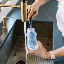 Silicone cleaning brush scrubbing a bottle with long handle, dark blue head