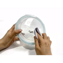 Round glass container lid being peeled with label marker, blue-tinted rim