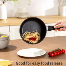 Black nonstick saucepan with handle, noodles coating the interior