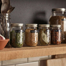 Clear spice jars with metal lids filled with herbs and seeds on a shelf