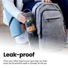 Portable personal blender held near a backpack, clear cup and gray lid