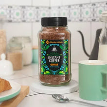 Instant coffee jar with black lid and green front label, brown coffee granules inside