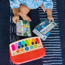 Red baby piano toy with colorful keys and a music card held above the screen