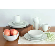 Ceramic dinnerware set in white with plates, bowls, and mugs arranged on a table.
