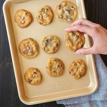 Natural aluminum loaf pan with round cavities and baked cookies, hand placing one