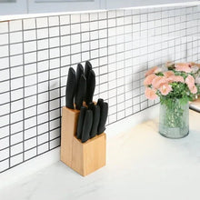 Bamboo knife block with black-handled knives on countertop near floral vase.