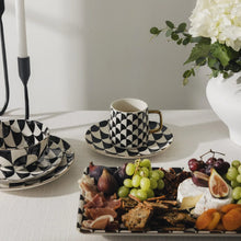 Black and white geometric stoneware mug with gold-tone handle on matching saucer