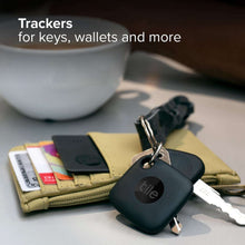Two black Tile trackers attached to keys and wallets on a table