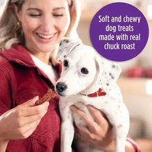 Person holding a brown bone-shaped dog treat while a white dog reaches