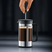 Stainless steel French press coffeemaker filled with brewed coffee, black handle