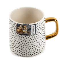14 fl oz dot stoneware mug in off-white with black speckles, gold-tone handle, product label
