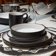 Black ceramic dinnerware with stacked plates and bowls, white interiors and dark rims