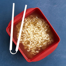 Red microwave ramen cooker tray filled with noodles and two white chopsticks