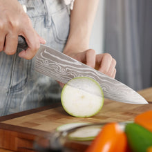 Chef knife with gray Damascus-pattern blade cutting a pale vegetable on a wooden board