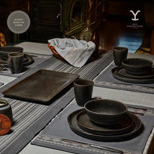 Black ceramic dinnerware set laid out on table with cups, bowls, and plates