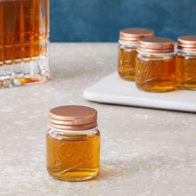 Mini mason jar shot glass with copper lid, amber liquid, on a light surface