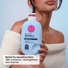Sensitive body lotion bottle held in hand, blue bottle with pink cap, label facing out