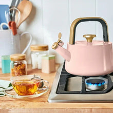 Rose ceramic stovetop tea kettle on gas burner with steaming hot tea