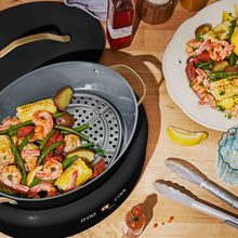 Black multi-cooker insert with steam holes, holding shrimp and vegetables