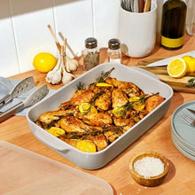 Stoneware baking dish with plastic lid, holding roasted chicken and lemons