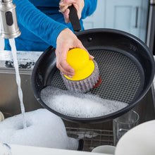 Handheld scrubber scrubbing a nonstick pan with yellow sponge head