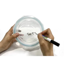 Round glass lid being marked by hands with a pen, blue-tinted rim