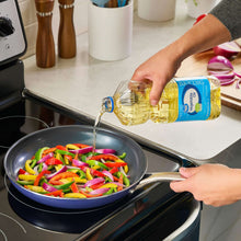 Vegetable oil bottle pouring into a skillet with sliced bell peppers