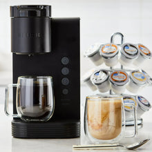 Coffee pod brewer with assorted flavored pods, glass mugs, and brewed coffee cup