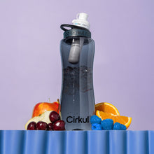 32oz gray water bottle with black lid and blue flavor cartridge, beside fruit