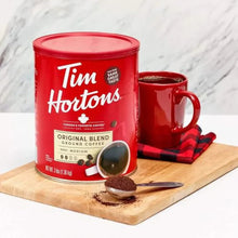 Tim Hortons Original Blend ground coffee can on wooden board with red mug and spoon.