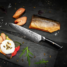 Damascus chef knife with black resin handle on dark countertop with plated fish