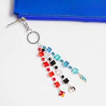 Beaded keychain charm with multicolor blocks, dangling accessories on a blue zipper pouch