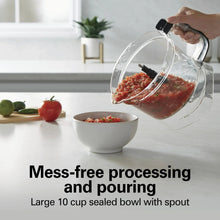 Clear food processor bowl tilted to pour chopped ingredients into a white serving bowl