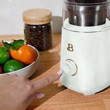White electric blade coffee grinder with a front power button being pressed