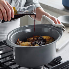 GreenPan slow cooker with lid on a counter, pouring sauce into the insert.